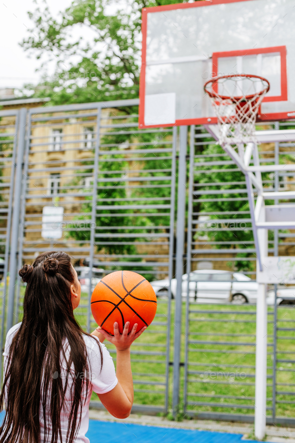 Young athletic woman is training to play basketball on modern outdoor